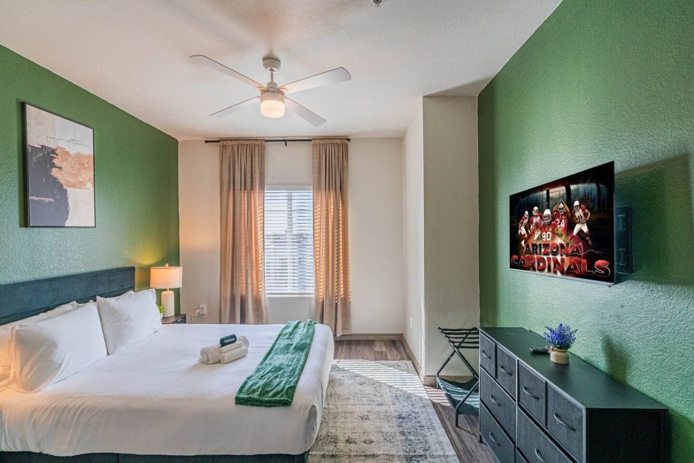 A hotel room with a bed, a ceiling fan, a television, and a window with curtains.
