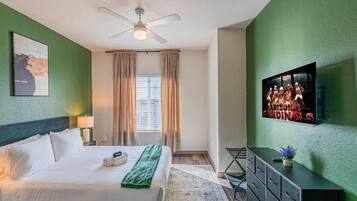 A hotel room with a bed, a ceiling fan, a television, and a window with curtains.