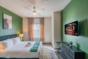 A hotel room with a bed, a ceiling fan, a television, and a window with curtains. - Near Stadium | Pool Gym Balcony Parking WD (Glendale)