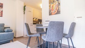 A modern living room with a grey sofa, a dining table with four grey chairs, and a kitchen in the background. - Modern 1BR 1LR Balcony City Centers (Vienna)