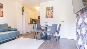 A modern living room with a grey sofa, a dining table with four chairs, and a kitchen in the background. - Modern 1BR 1LR Balcony City Centers (Vienna)