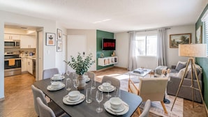 A modern living space with a dining area, kitchen, and a flat-screen TV mounted on the wall. - Near Old Town | Pool+Gym+Balcony+Parking+WiFi+WD (Scottsdale)