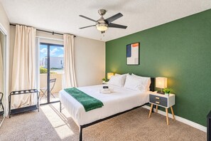 A hotel room with a bed, a ceiling fan, a nightstand with a lamp, a green wall, and a view through a sliding door. - Near Old Town | Pool+Gym+Balcony+Parking+WiFi+WD (Scottsdale)