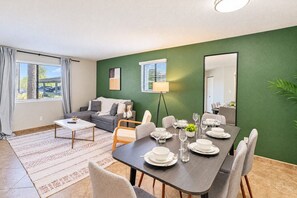 A modern living room with a dining table set for four, a sofa, and a large window with curtains. - Near Old Town | Pool+Gym+Balcony+Parking+WiFi+WD (Scottsdale)