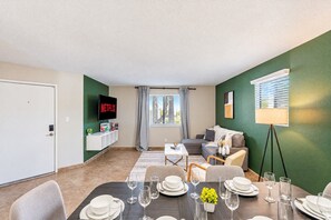 A modern living room with a dining area, green walls, a flat-screen TV, and a window with curtains. - Near Old Town | Pool+Gym+Balcony+Parking+WiFi+WD (Scottsdale)