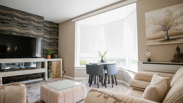 Ein Wohnzimmer mit Fernseher, Sitzmöbeln, Kamin und großem Fenster.