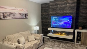 Ein modernes Wohnzimmer mit Sofa, Flachbildfernseher, Kamin und einer an der Wand befestigten Ablagefläche.