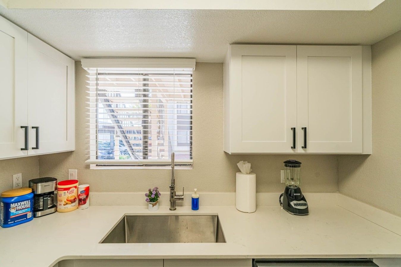 A small kitchenette with a sink, a window with blinds, and cabinets.
