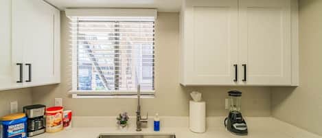Una pequeña kitchenette con un lavamanos, una ventana con persianas y armarios.