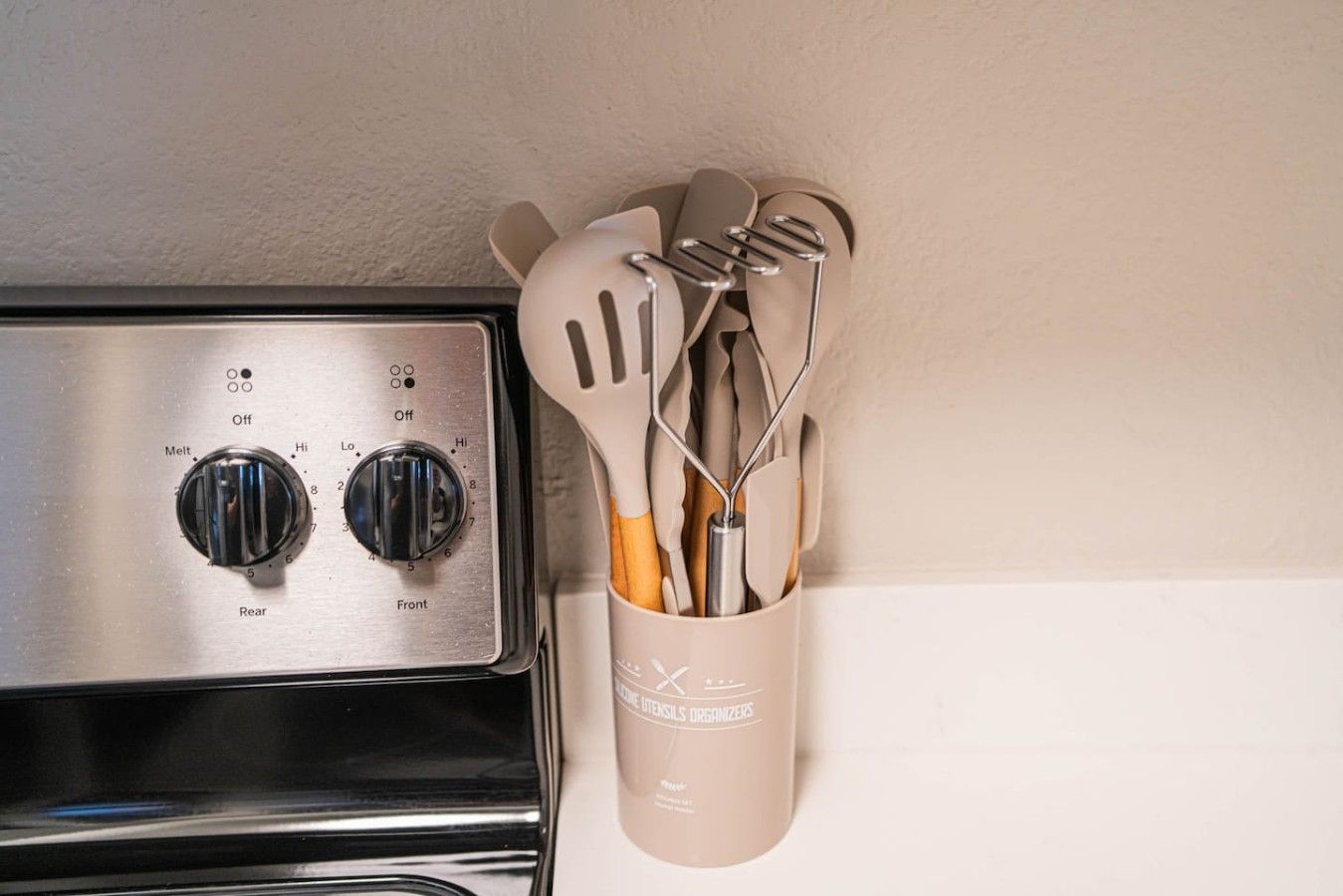 A kitchen with a stove and a utensil holder with spatulas and whisks.
