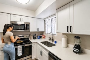 Una cocina moderna con armarios blancos, microondas, estufa, fregadero y licuadora.