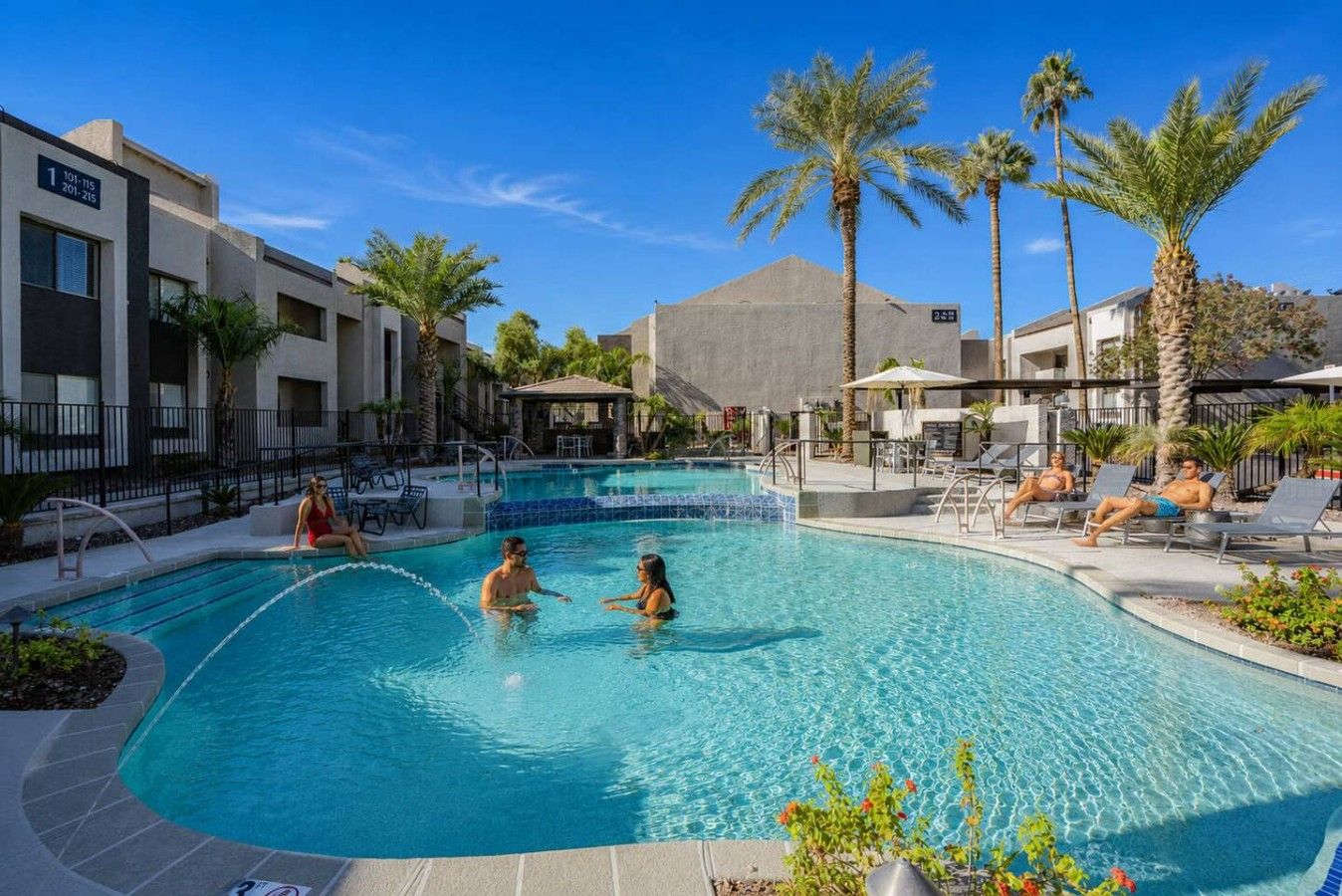 A swimming pool with lounge chairs and palm trees, surrounded by modern buildings.