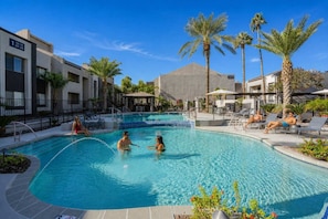 A swimming pool with lounge chairs and palm trees, surrounded by modern buildings.