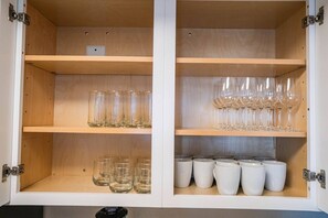 A cabinet with three shelves; the top shelf holds a laptop, the middle shelf has clear glasses, and the bottom shelf contains white mugs.