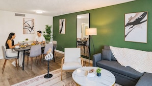 A dining area with a table and chairs, a sofa, a floor lamp, and artwork on the walls. - Bright Urban Retreat | Balcony Gym Washer/Dryer (Scottsdale)