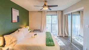 A hotel room with a bed, a ceiling fan, a window with curtains, and a view of the outdoors. - Bright Urban Retreat | Balcony Gym Washer/Dryer (Scottsdale)
