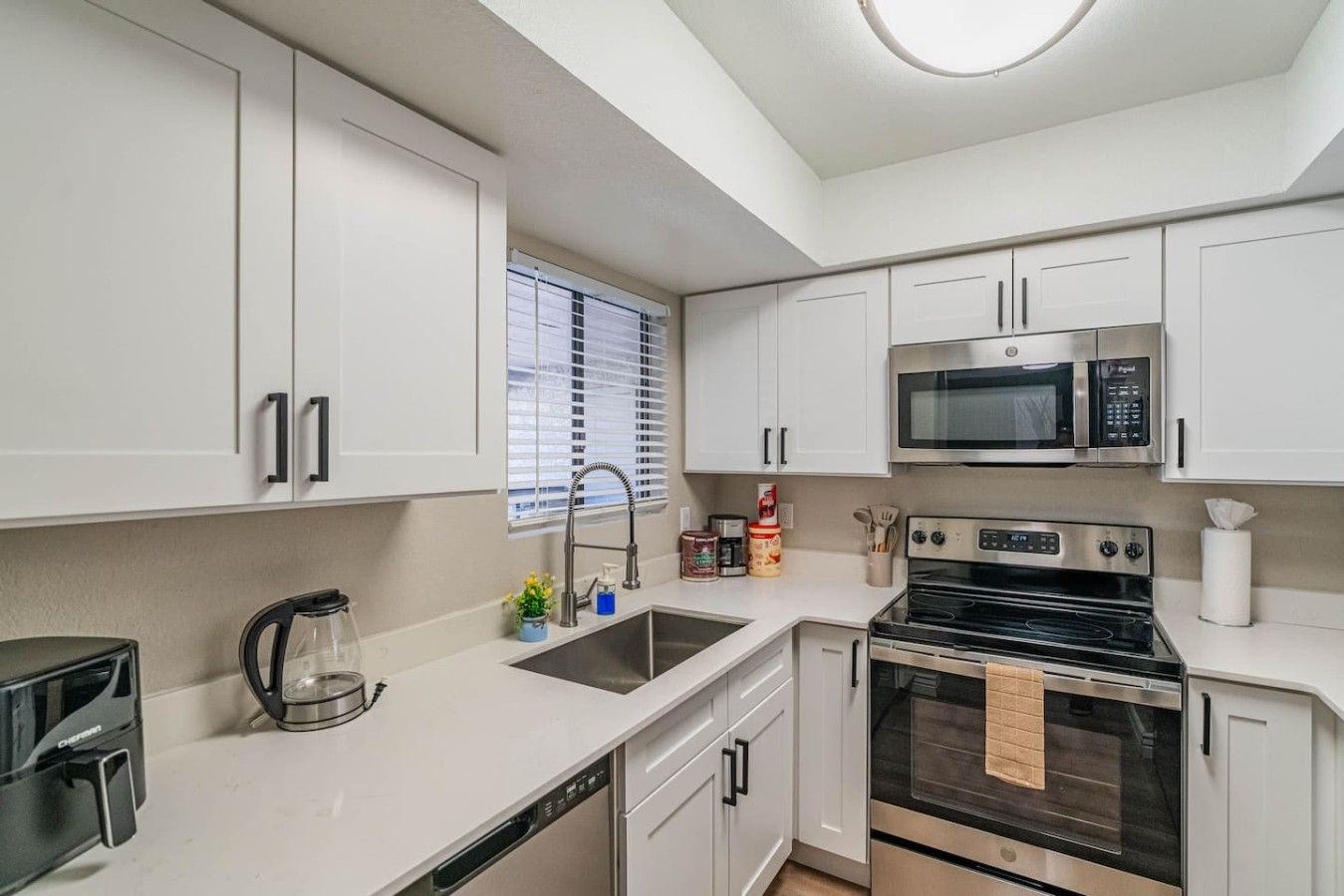 A modern kitchen with white cabinets, a stainless steel microwave, an oven, and a dishwasher.