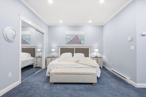 A bedroom with a large bed, two bedside tables with lamps, a mirror, and artwork on the wall. - Riverview Retreat: Guest Suite (Groton)