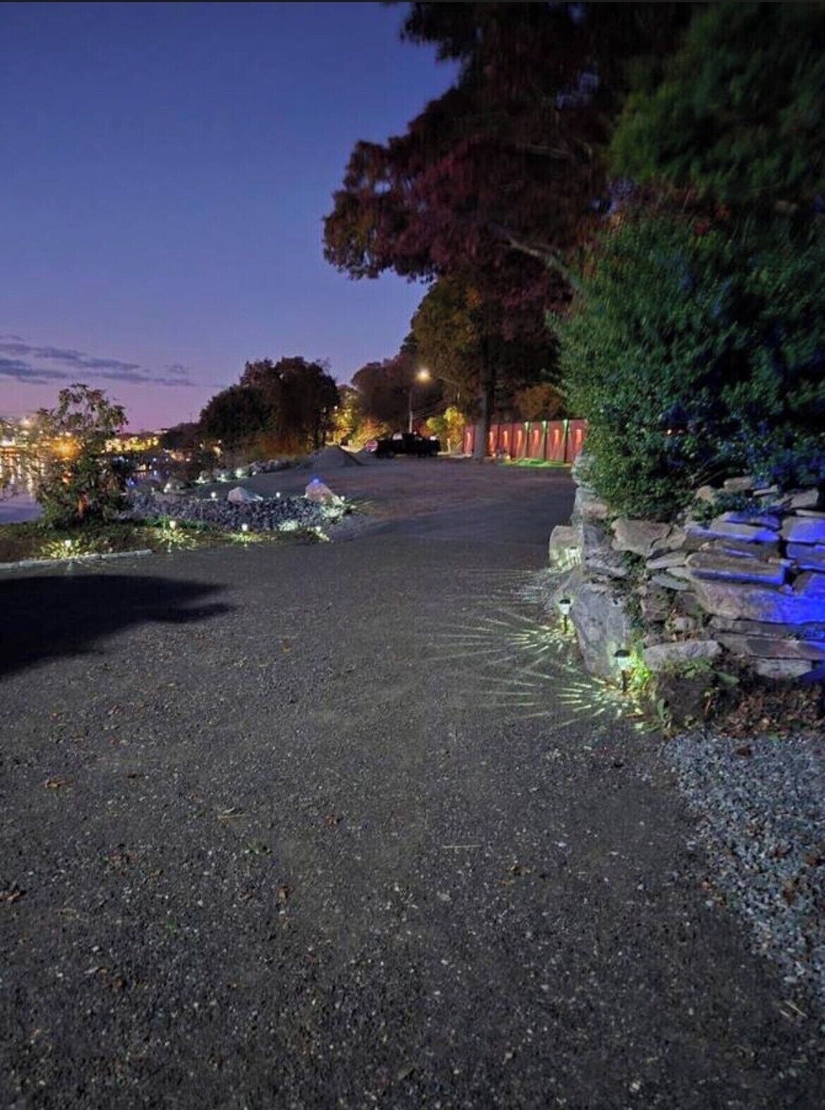 A paved pathway leading to a stone wall with a small water feature on the left.