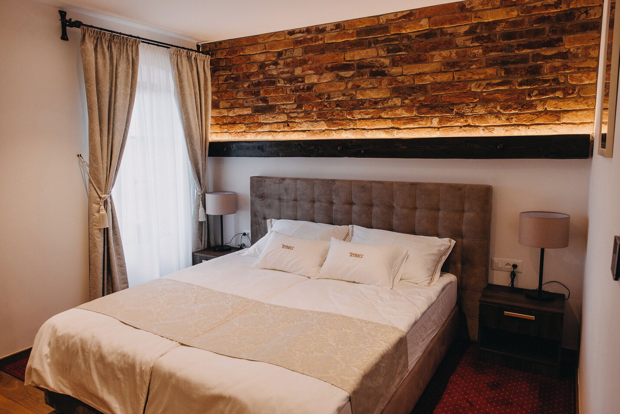 A bedroom with a brick wall, a bed with white bedding, and two bedside tables with lamps.
