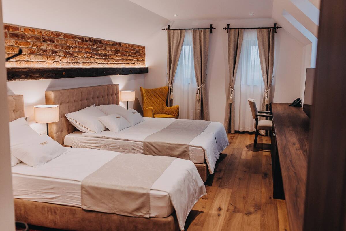 Een hotelkamer met twee bedden, een houten vloer, een accentmuur van baksteen en een bureau met een stoel.