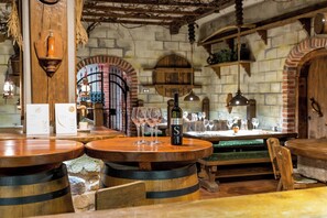 A rustic bar with wooden barrels, a bottle of wine, and glasses on a wooden table.