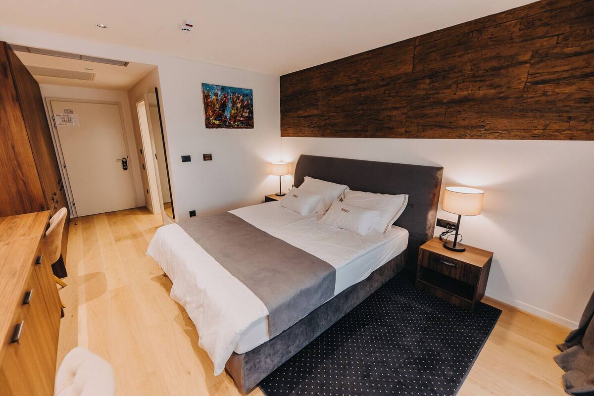 Een slaapkamer met een bed, nachtkastjes, een houten hoofdbord, een deur en een schilderij aan de muur.