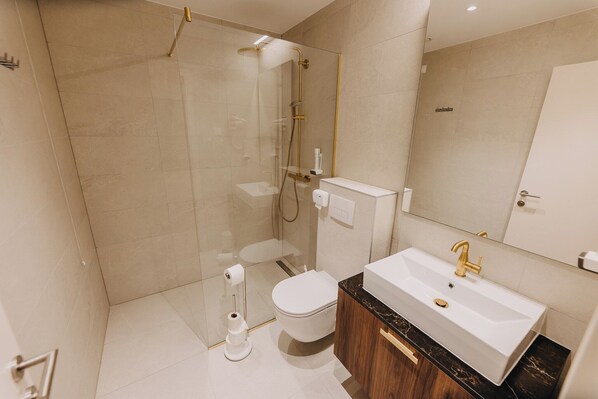 A modern bathroom with a glass-enclosed shower, a white toilet, and a sink with a marble countertop.