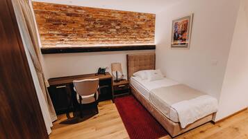 A bedroom with a wooden desk, a bed, a red rug, a brick wall, and a painting.