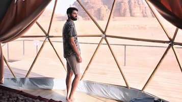 A tent with a bed and a small table, a view of a desert landscape.
