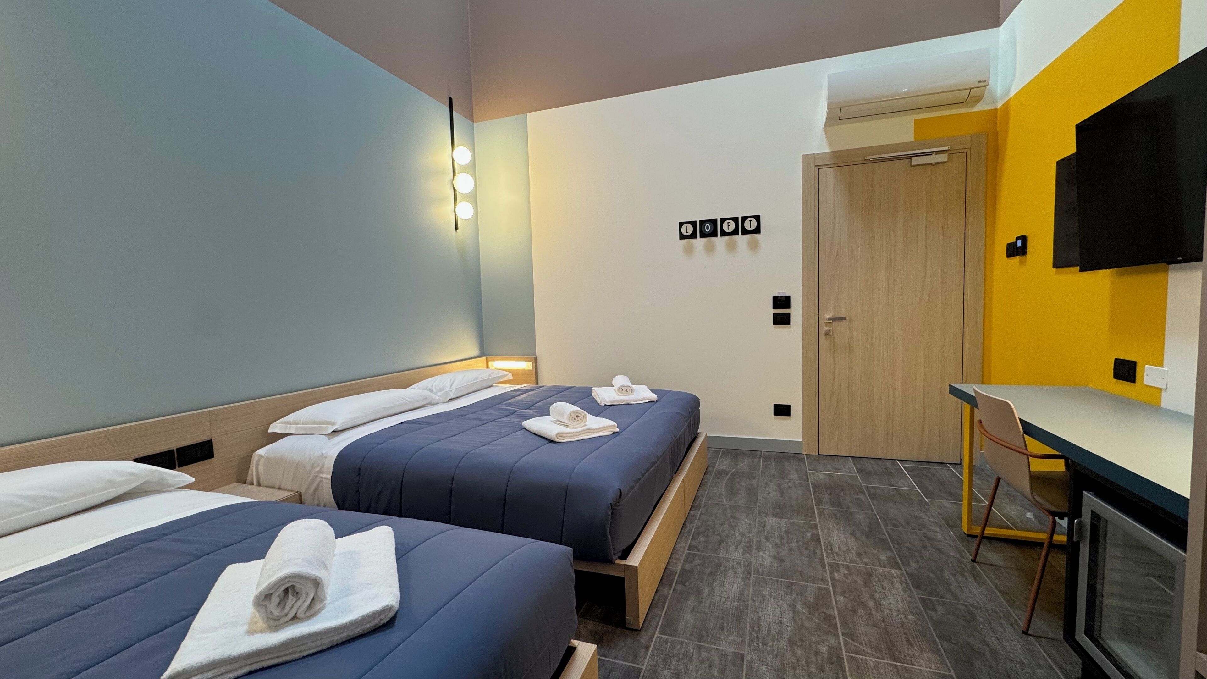 Une chambre d’hôtel avec deux lits, un bureau, une chaise, une télévision et une porte.