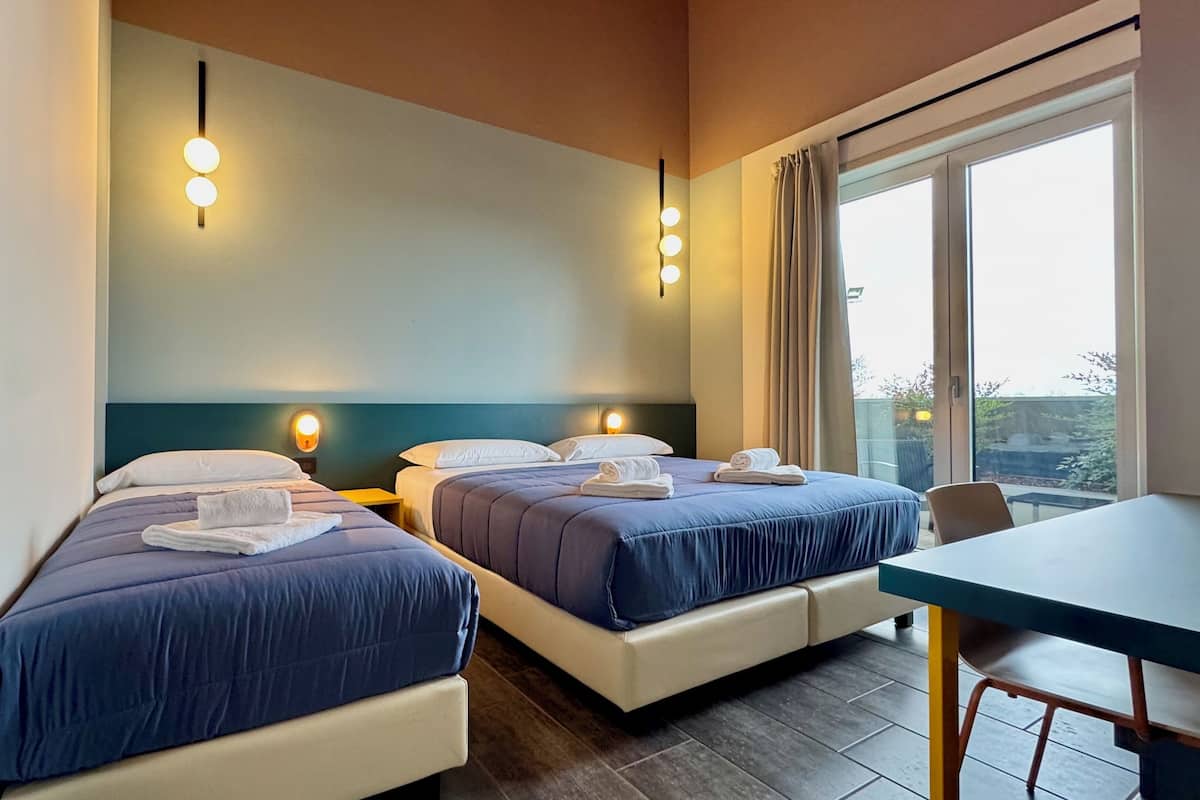 A hotel room with two beds, a table, and a large window.