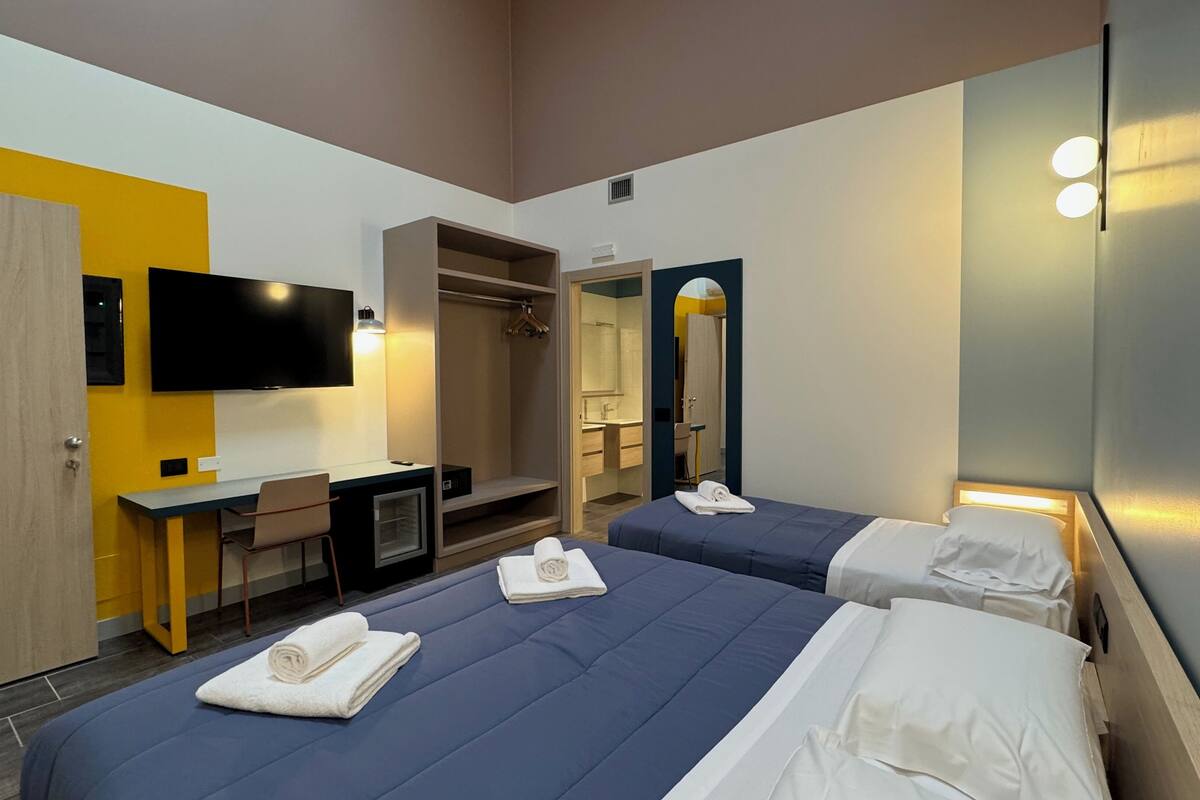 A hotel room with two beds, a desk, a TV, and a shower area.