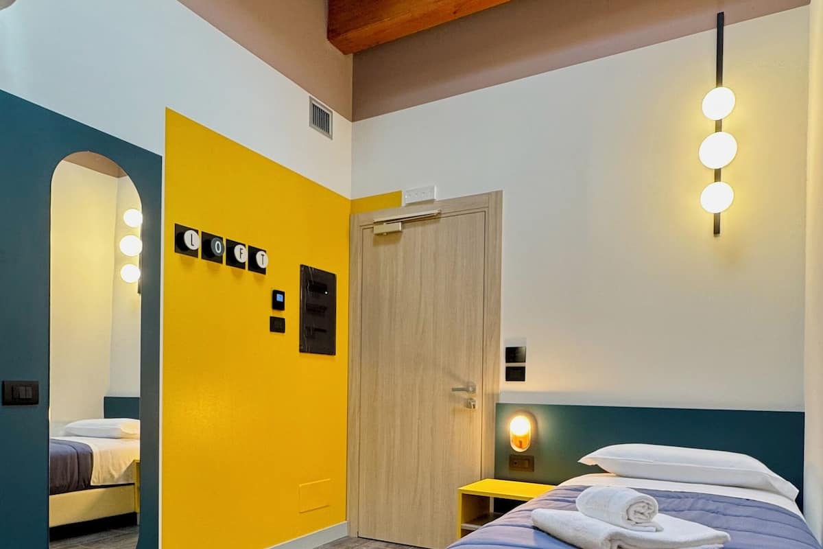 A modern bedroom with a large bed, a mirror, a wardrobe, and a nightstand with a lamp.