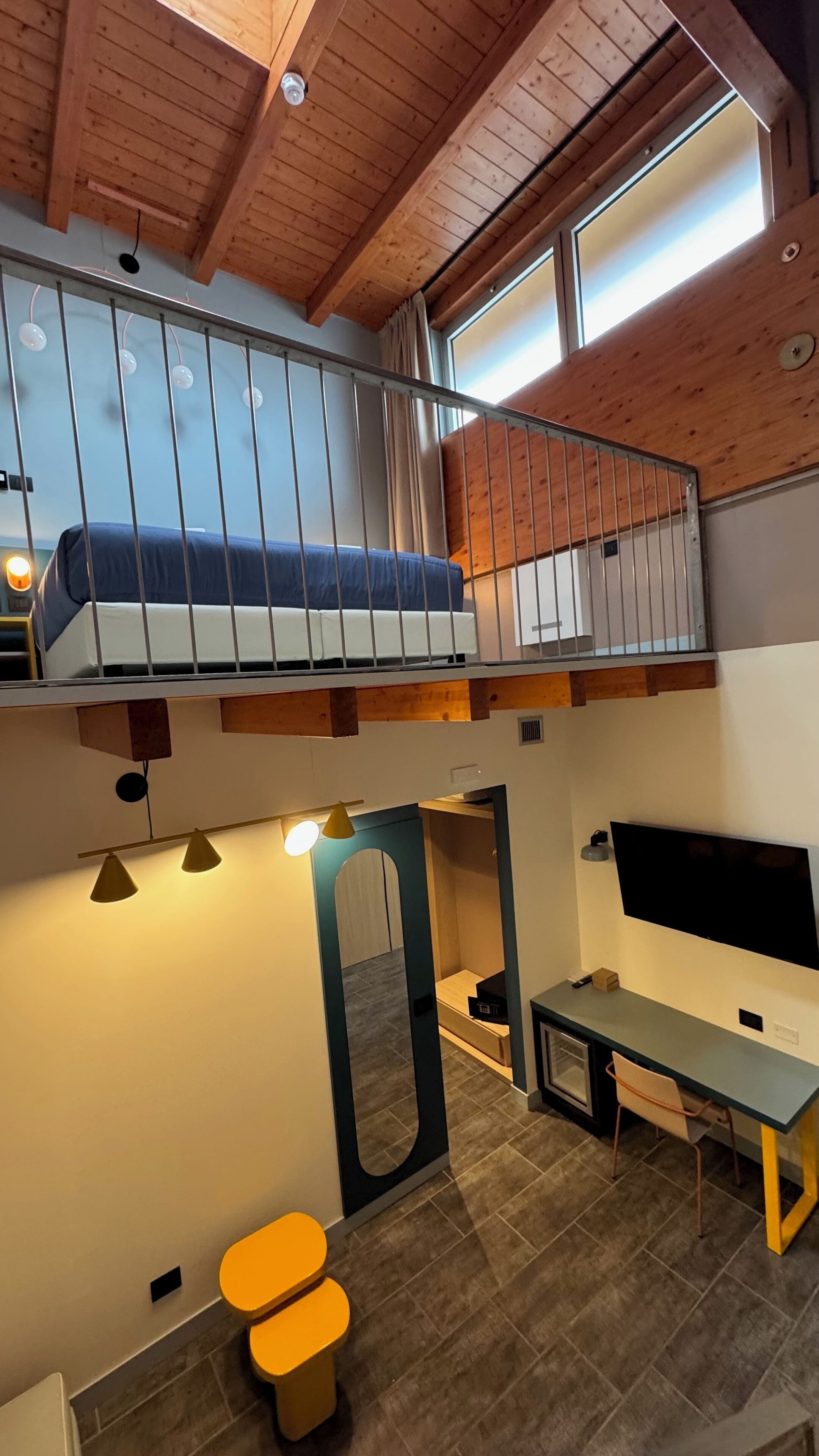 A loft-style bedroom with a bunk bed, a desk, a chair, and a TV.