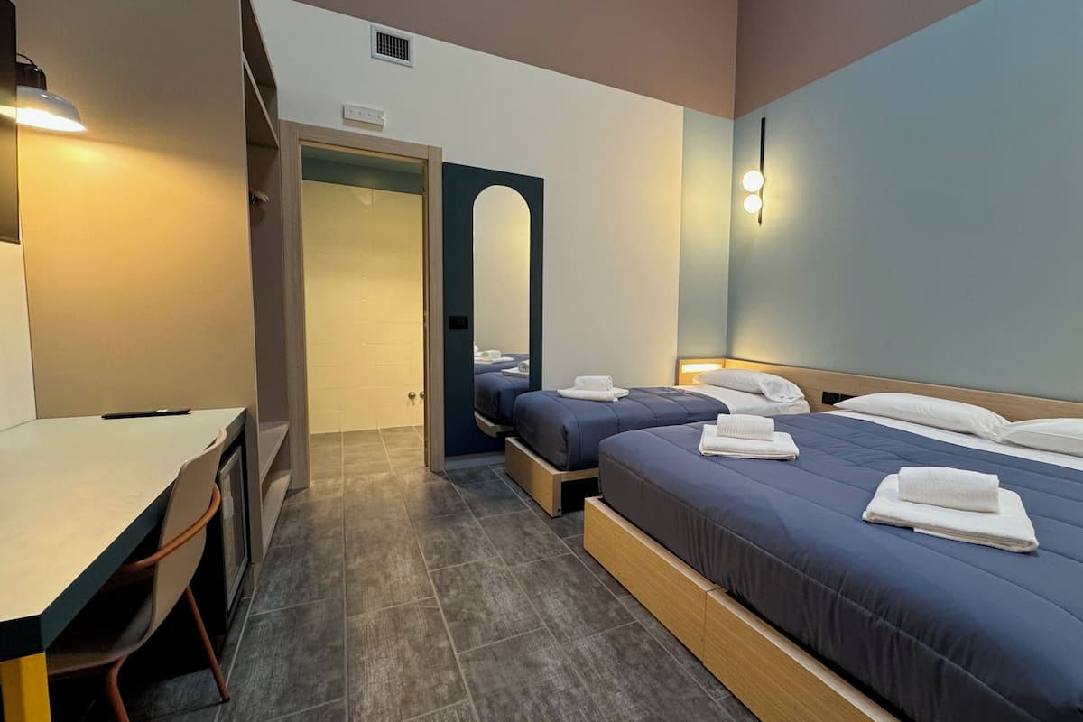A hotel room with two beds, a desk, and a mirror.