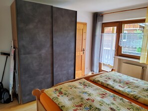A room with a bed, a wardrobe, a radiator, a window with curtains, and a door.