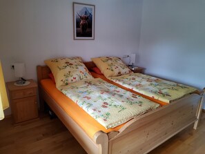 Parivuode kukkakuosisilla vuodevaatteilla, yöpöytä lampun kanssa ja seinällä oleva kehystetty kuva.