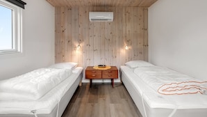 Una habitación pequeña y acogedora con dos camas individuales, techo de madera, unidad de aire acondicionado y una mesita con lámpara.