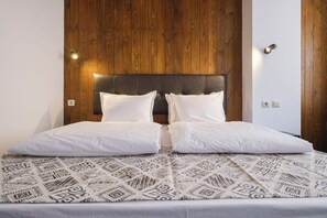 A double bed with a patterned bedspread, a wooden headboard, and two wall-mounted lights. - Hotel Razlog (Razlog)