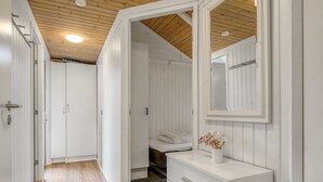 A hallway with white walls and wooden flooring leading to a bedroom with a bed and a dresser with a mirror.