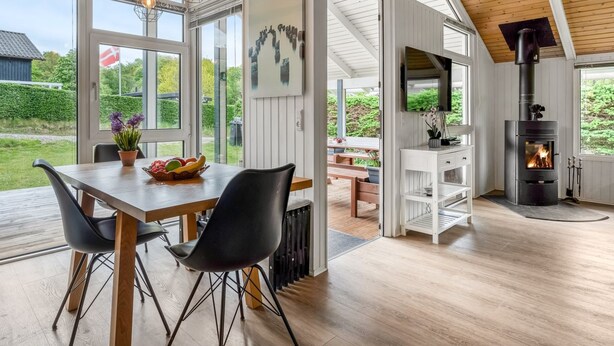 A modern interior with a dining area, white walls, wooden ceiling, and a wood-burning stove.