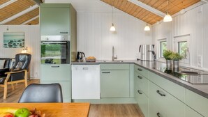 A modern kitchen with a dishwasher, oven, and coffee maker. There is a dining area with a table and chairs.