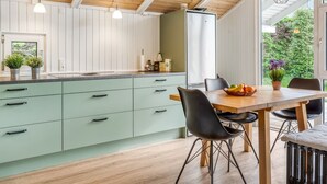 A modern kitchen with a wooden ceiling, green cabinets, and a dining area with a table and chairs.
