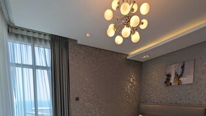 A modern bedroom with a large bed, a ceiling light fixture, and a view through the window. - Oceanview apartment with FREE parking in Hoora Manama (hoora manama)
