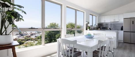Una cocina moderna con armarios blancos, un refrigerador de acero inoxidable y un ventanal con vistas a un paisaje urbano.