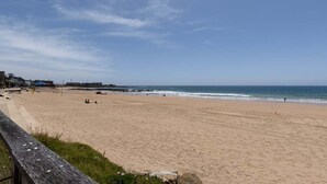 Una amplia playa de arena con un camino de madera y algunos sombrillas.