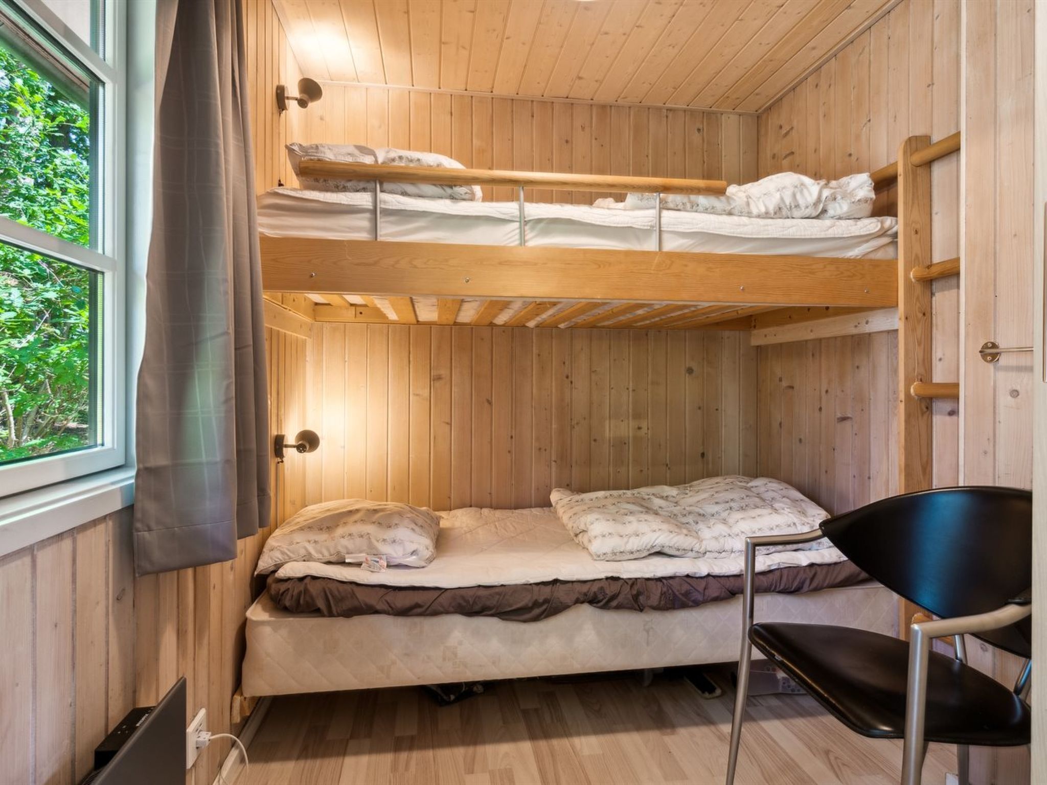 Een slaapkamer met een stapelbed, een raam, een stoel en een wandlamp.