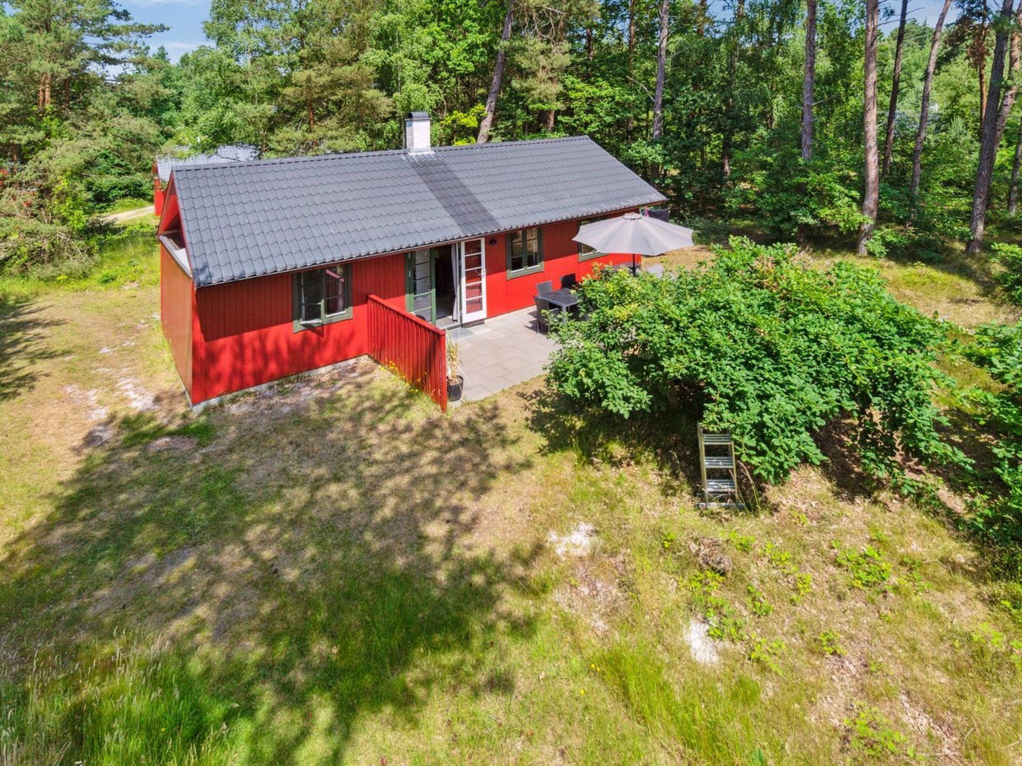 Une maison rouge avec un toit gris, entourée de verdure.