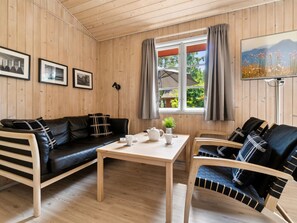 A cozy room with wooden walls, a black leather sofa, a wooden table with a plant, and a chair with a striped cushion. - "Wale" - 100m from the sea by Interhome (Nexø)
